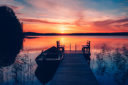 Sunset on a lake. Wooden pier with fishing boat at sunset in Finland. Beautiful summer landscape.