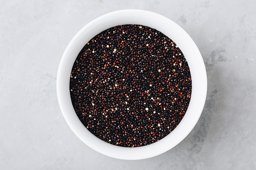 Quinoa. Raw black quinoa seeds in bowl on gray stone background, top view, copy spaceQuinoa. Raw black quinoa seeds in bowl on gray stone background