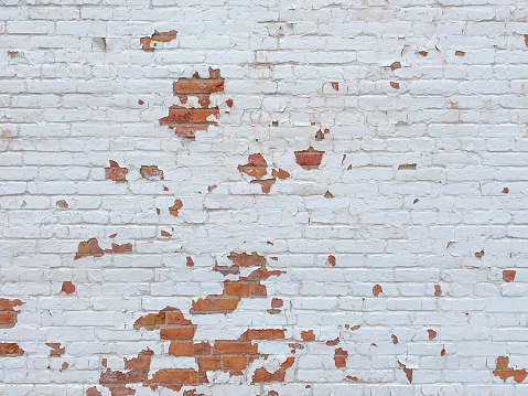 Red brick wall painted white with flaking paint chips