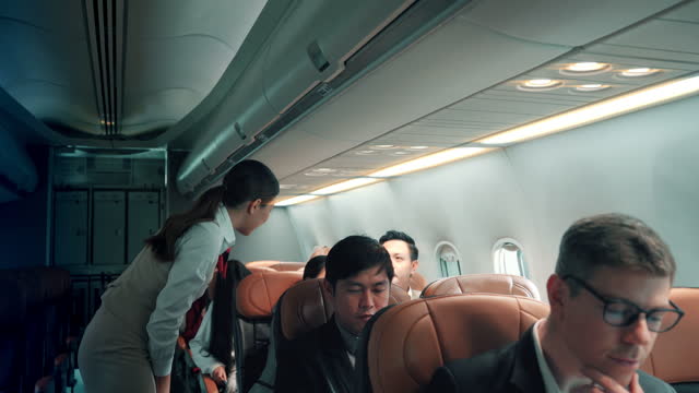 Female flight attendants check the preparations with passengers before flight traveling and talking to businessman while using laptop. Air stewardess greeted a tourist on airplane.