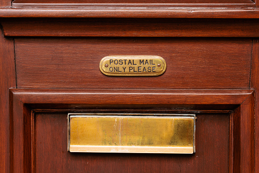 Part of an old door with brass mail slot and postal mail only sign.