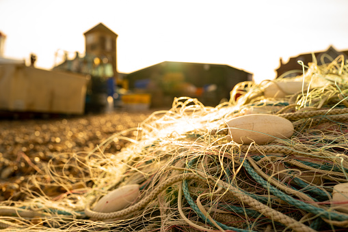 Shallow focus of beach netting and net floats seen on a beach during sunset. The distance shows a seaside town with a deep history in fishing.