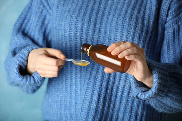 istock Woman pouring cough syrup into spoon on light blue background, closeup 1453294952