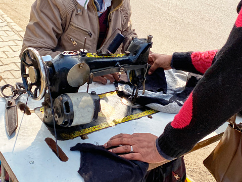 Stock photo showing an outdoor, roadside sewing business with old fashioned, manual sewing machine on being used on pavement.