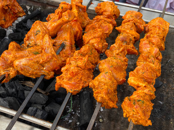 istock Full frame image of uncooked chicken kebabs, marinated raw chicken breast pieces on metal skewers, lying in rows over hot charcoal embers, elevated view 1453305969