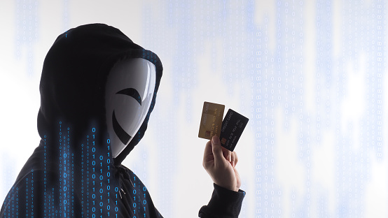 Hacker man and credit cards in hand. Represent credit cards personal data stolen by anonymous man in Black hood shirt. Credit cards data security and Cyber crime digital. Money transection unsecured.