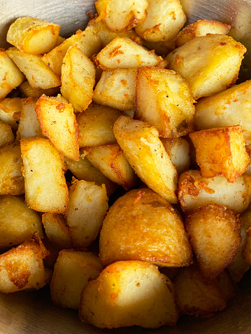 Stock photo showing an elevated view of the inside of a metal bowl with a pile of golden, freshly cooked roast potatoes.