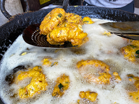Stock photo showing close-up view of an unrecognisable chef turning popular breakfast snack of golden Medu vada (soft fritters) in boiling oil, savoury doughnut fritters made from Vigna mungo (black lentil) batter.