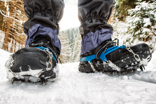 Crampons on black hiking boots in snowy forest. Hiking in winter