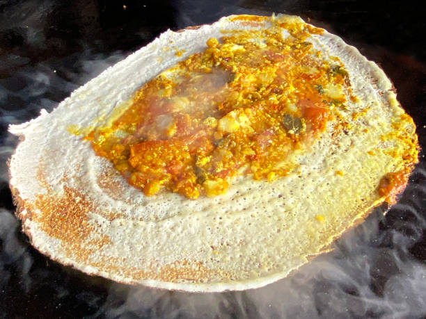 Full frame image of dosa pancake, traditional Indian street food being cooked on outdoor stove, savoury filling of masala potato, onions and coriander, smoking, hot oven top, elevated view, focus on foreground Stock photo showing close-up, elevated view of a savoury filling of masala potato, onions and coriander on cooked dosa pancake a traditional Indian street food. Dosa stock pictures, royalty-free photos & images