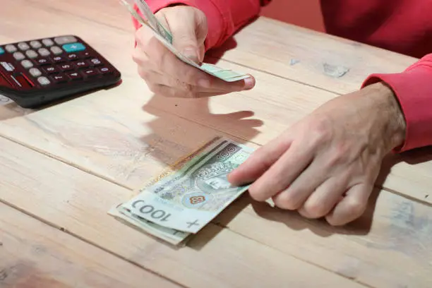 counting Polish zloty cash over the table by a person in a red sweatshirt