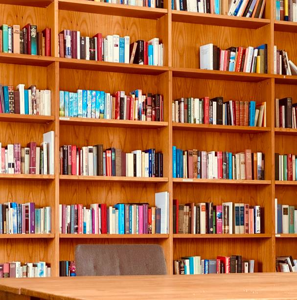 istock Library, table and fully packed wooden shelves 1453311121