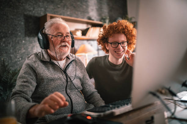 abuelo y nieto sentados alrededor de la mesa en casa y usando la computadora - relación humana fotografías e imágenes de stock