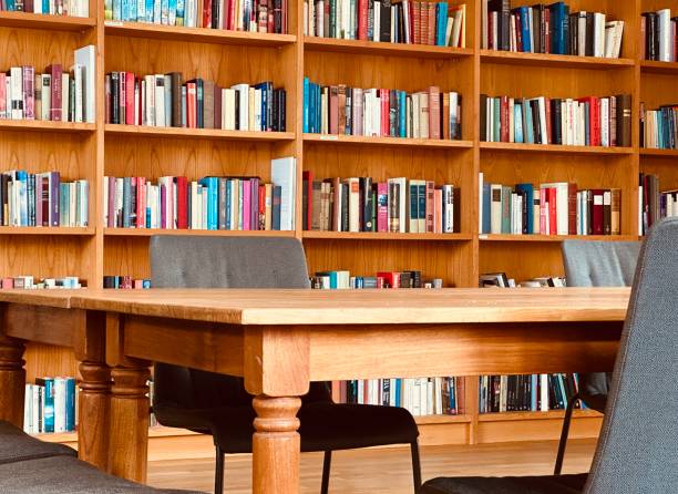 istock Library, table and fully packed wooden shelves 1453311179