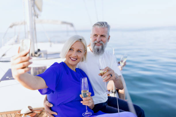 Loving couple sailing on a yacht and drinking champagne while enjoying the summer Smiling group of friends traveling on a yacht and drinking champagne. Mature adult friends sitting on sailboat's deck and drinking champagne enjoying the view yacht selfie stock pictures, royalty-free photos & images