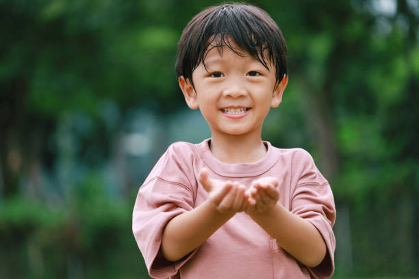 istock Little Asian boy with opened hands standing at the greenery park 1453313988