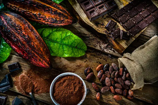 Overhead view of organic cocoa pods, cocoa beans cocoa powder shot on rustic wooden table. High resolution 42Mp studio digital capture taken with SONY A7rII and Zeiss Batis 40mm F2.0 CF lens