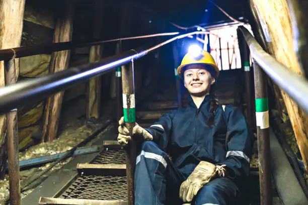 Portrait of a miner looking at the camera smiling as she walks down the stairs of a coal mine.