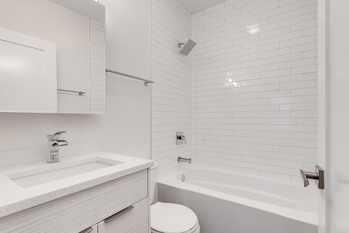 An all white small bathroom with chrome hardware. The bathtub / shower is lined with white subway tiles.