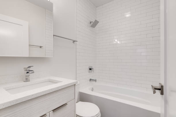 A white bathroom with a tiled shower. An all white small bathroom with chrome hardware. The bathtub / shower is lined with white subway tiles. bathtub stock pictures, royalty-free photos & images