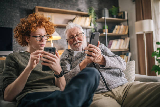 grandfather and grandson having fun and looking a smart phone - senior adult technology child internet imagens e fotografias de stock