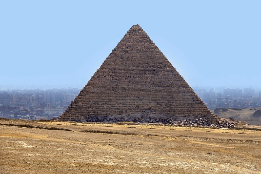 Giza, Egypt, April 16, 2022: View of the Pyramid of Menkaure.  In the background is Cairo covered by smog. The pyramid field of Giza is listed as UNESCO World Heritage Site.