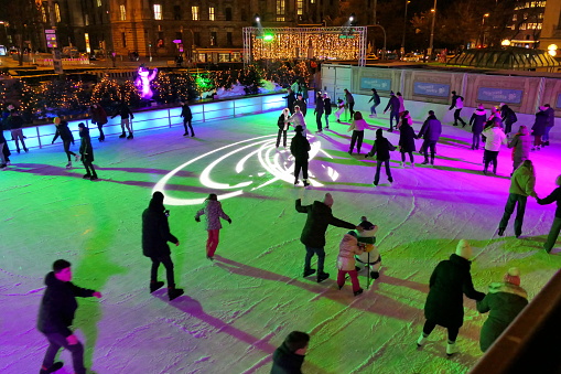 Munich, Germany - December 2022: Karlsplatz Stachus skating rink in the evening. Many people having fun at this particular popular Christmas site in the center of Munich. In the summer is there a fountain which is a popular meeting place for residents and tourists.