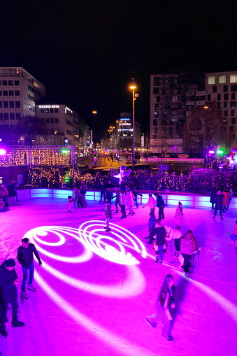 Munich, Germany - December 2022: Karlsplatz Stachus skating rink in the evening. Many people having fun at this particular popular Christmas site in the center of Munich. In the summer is there a fountain which is a popular meeting place for residents and tourists.
