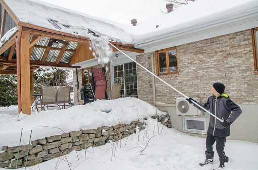 Teenage boy shoveling snow from patio rooftop  during a day of winter