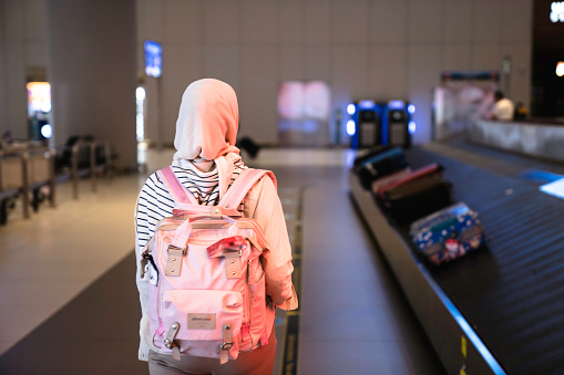 muslim Woman picking up suitcase on luggage conveyor belt carousel in the baggage claim at airport
