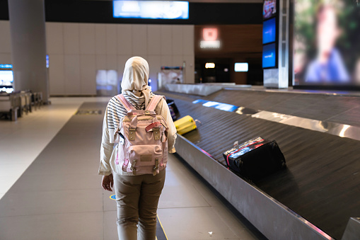 muslim Woman picking up suitcase on luggage conveyor belt carousel in the baggage claim at airport