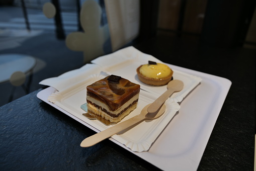 A creamy caramel cake and a lemon pie served on two paper plates with two wooden spoons in a French patisserie in Paris