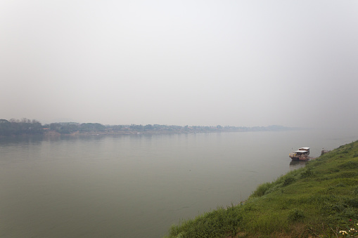 Downstream riverside panorama at Mekong river in early morning and sunrise in Chiang Kham with border to Laos in morning with haze and smog in air in north of Thailand