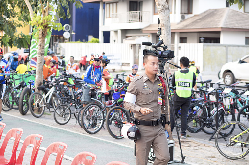 Thai police officer is walking in Nakhon Phanom on  street at promenade along Mekong river in morning. In background are people and many bicycles for locqal public cycling and health day event
