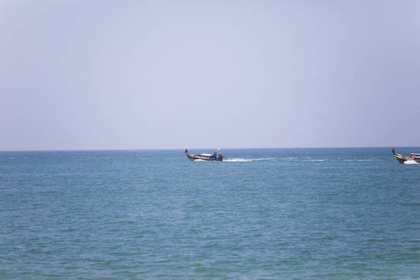 Thai longboat is navigating in Andaman Sea in front of Krabi beach in south Thailand. Another one is approaching at right side