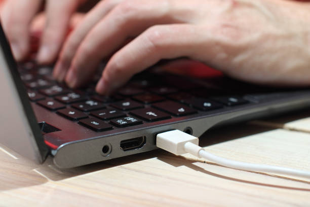 istock white usb cable in laptop port with hands on keyboard 1453331108