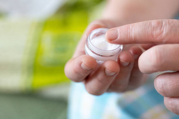 Women's hands take testosterone cream from the package and study its texture.