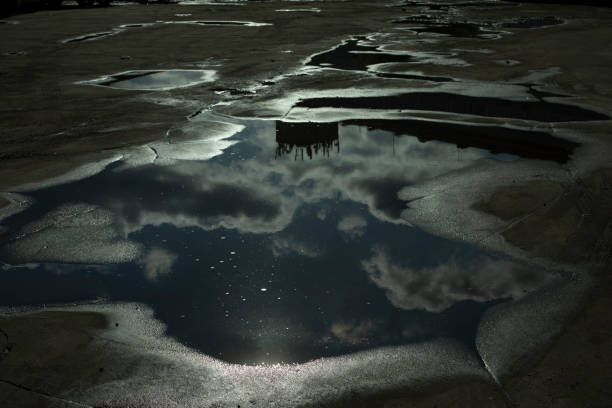 Puddle on pavement. After rain. Road in pits. Reflection of sky in puddle.