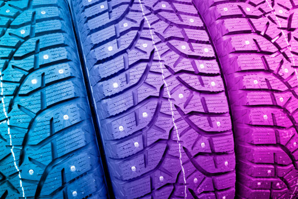 istock Winter studded tire. Winter car tires background. Tire stack background. Tyre protector close up in pink and blue tones. Black studdable winter tyre profile. Car tires in a row 1453337187