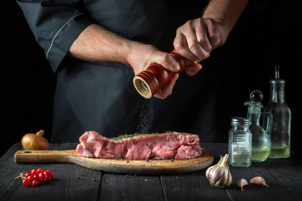 le chef prépare de la viande de veau crue. avant la cuisson, le chef ajoute du poivre au bœuf. un plat national est en cours de préparation dans la cuisine du restaurant - veal calf meat baking photos et images de collection