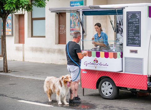 Bucharest, Romania - August 2022: Man with a dog pet buying ice cream from a mobile truck street vendor in the center of Bucharest.
