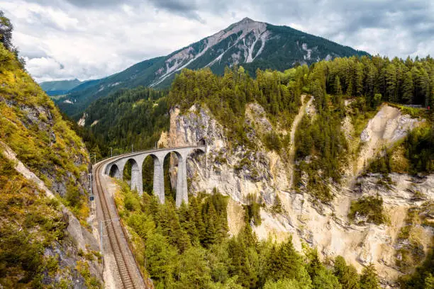 Landwasser Viaduct in Filisur, Switzerland. Aerial view of railway in mountains, Alpine landscape in autumn. Scenery of railroad bridge in forest, landmark of Swiss Alps. Nature and travel theme.