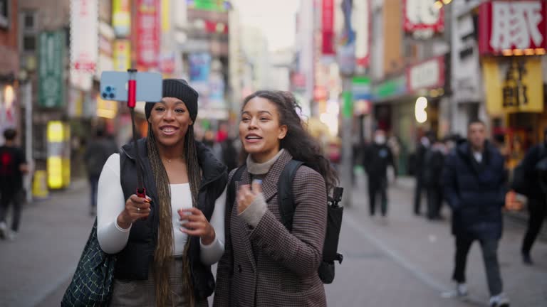 Two multi-racial female tourist friends taking selfies and videos while exploring the city In Shibuya Tokyo