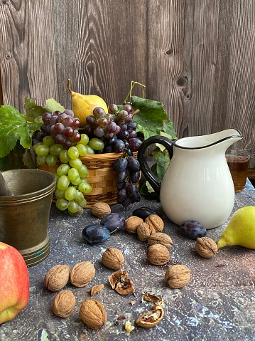 On the stone table there is an old copper mortar, nuts, a jug of wine, grapes and fruits