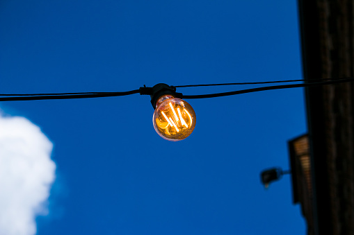 Close up of an Edison-style filament on a light bulb against a cloudy sky. Energy crisis.