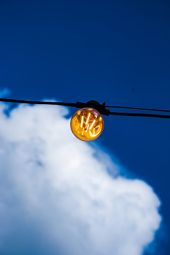 Close up of an Edison-style filament on a light bulb against a cloudy sky. Energy crisis.