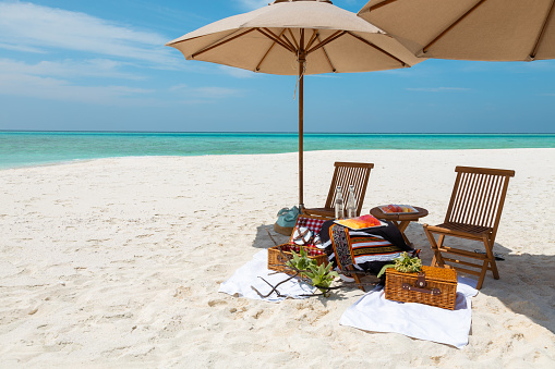 Maldives beach picnic with fruits and parasols on honeymoon sandbank with turquoise lagoon