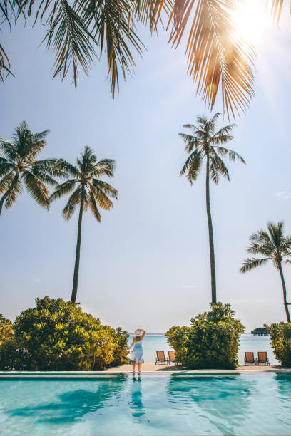 熱帯のアイランドリゾートホテルのモルディブのプールのそばに立つ女性 ヤシの木のあるビーチ - vacations infinity pool relaxation swimming pool ストックフォトと画像