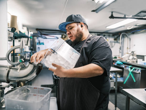 Young Mexican male chef working in restaurant kitchen Young Mexican male chef working in restaurant kitchen. He is wearing usual kitchen attire with apron and baseball cap. Interior of industrial kitchen of a busy restaurant. ice machines stock pictures, royalty-free photos & images