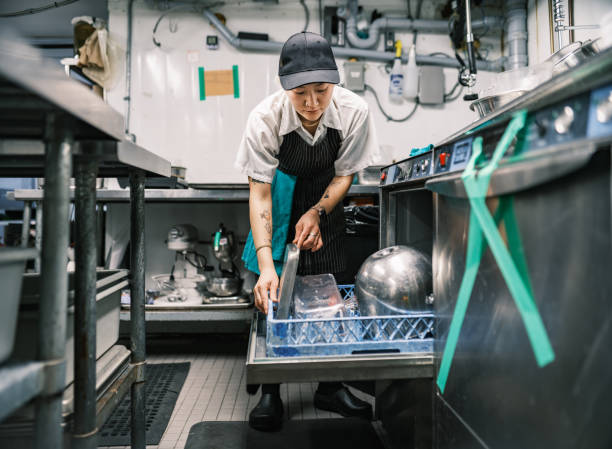 Young Korean female chef working in restaurant kitchen Young Korean female chef working in restaurant kitchen. She is wearing usual kitchen attire with apron and baseball cap. Interior of industrial kitchen of a busy restaurant. dishwasher stock pictures, royalty-free photos & images